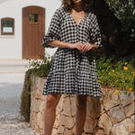 Woman wearing a black and white gingham mini dress with a button-down front, tiered skirt, and mid-length sleeves.