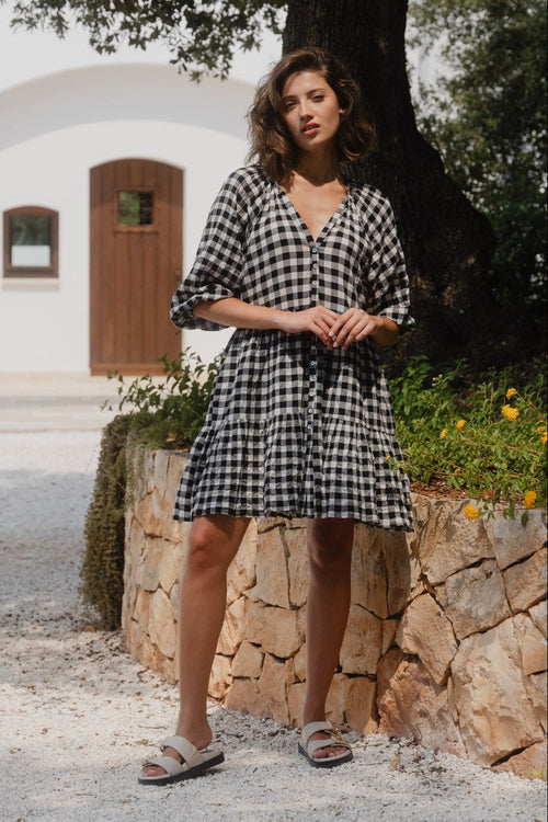 Woman wearing a black and white gingham mini dress with a button-down front, tiered skirt, and mid-length sleeves.