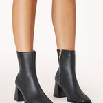 Black ankle boots with block heels worn by a person on a white background