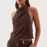 A woman modeling a dark brown sleeveless halter crop top and matching wide-leg trousers with a belt, against a plain light gray studio background.