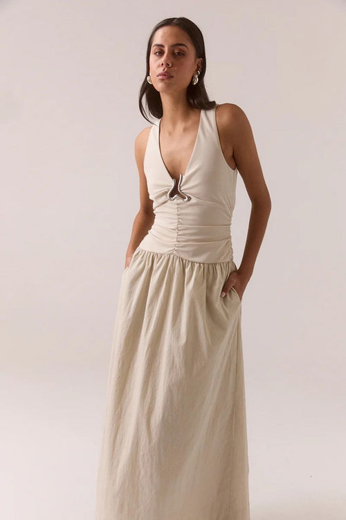 Woman wearing a beige halter neck dress against a plain background