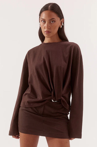 A woman modeling a dark brown long-sleeve top and matching mini skirt set against a plain light background.