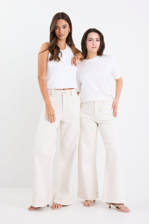 Two women wearing white outfits standing side by side on a white background