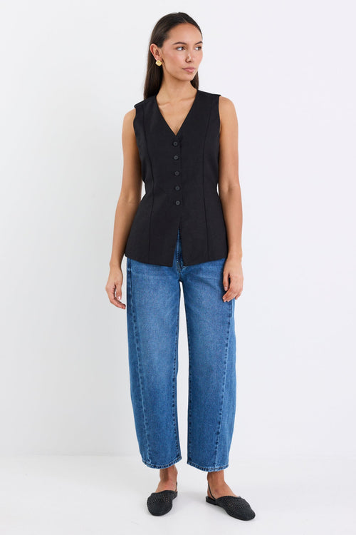 Woman wearing a black sleeveless top and blue jeans on a white background