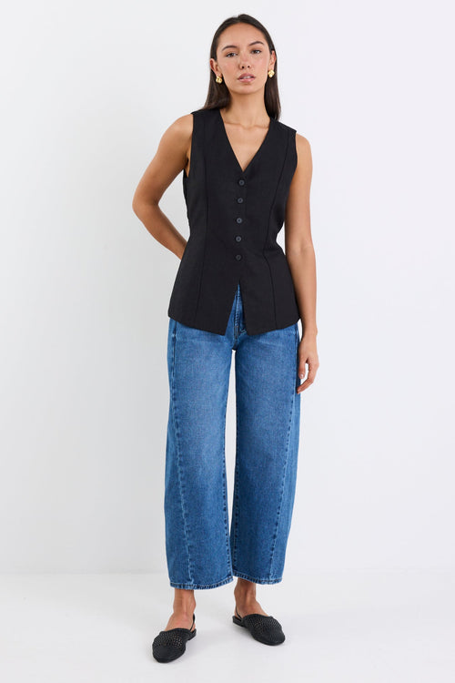 Woman wearing a black sleeveless top and blue jeans on a white background