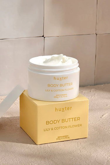 An open white jar of Huxter body butter in the scent 