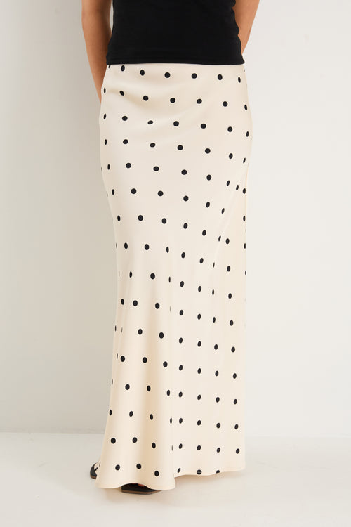 the model wears a cream maxi skirt with black polka dots and a black tank top