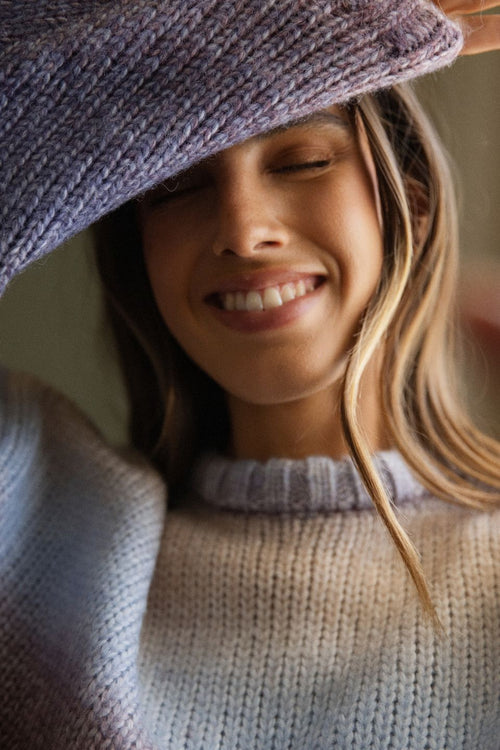 Woman wearing a knitted hat and sweater, smiling.