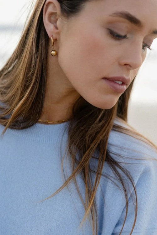 Close-up of a woman wearing gold earrings and a light blue sweater.