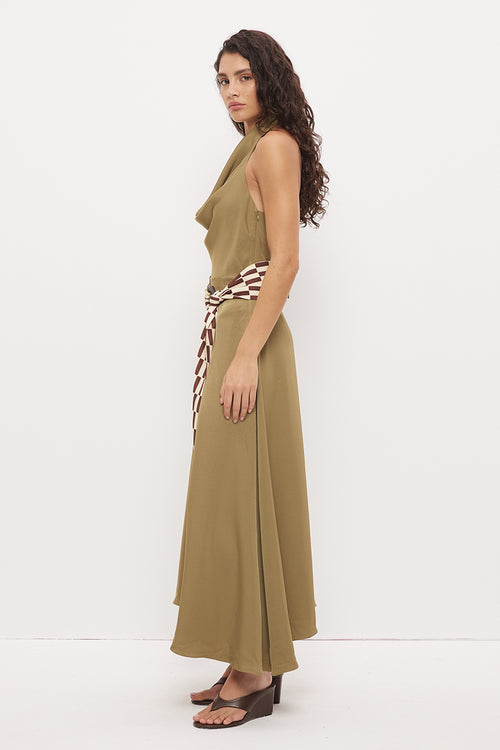 A woman modeling a sleeveless olive green maxi dress with a brown and white patterned tie belt, shown from a side profile against a plain white studio background.