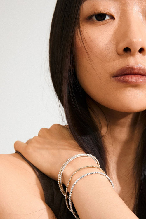 Close-up of a woman wearing multiple bracelets on her wrist against a neutral background