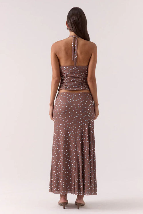 Woman wearing a ruched halter neck top in brown and blue polka dots with the matching skirt