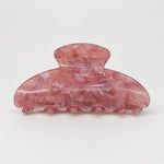 A translucent pink hair claw clip with a marbled pattern, photographed on a seamless light gray background.