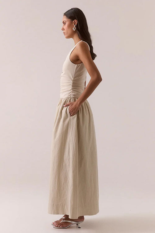 Woman wearing a beige sleeveless dress against a plain background