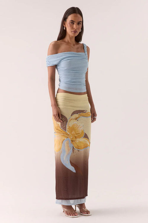 Woman wearing a light blue off-shoulder top and a long, patterned skirt on a white background