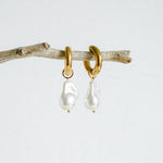 A pair of gold-toned hoop earrings featuring dangling baroque freshwater pearls, suspended from smooth, polished hoops for an elegant and organic look