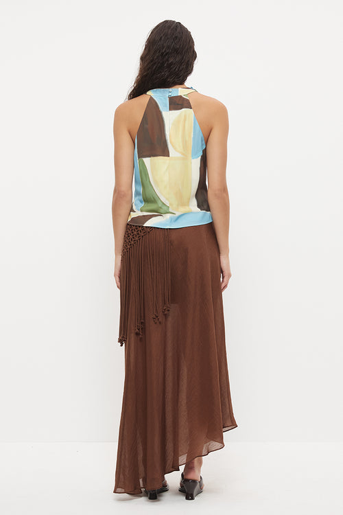 A woman shown from the back wearing a sleeveless halter-neck top with an abstract geometric print in brown, cream, light blue, and green, paired with a long brown pleated skirt, against a plain white studio background.