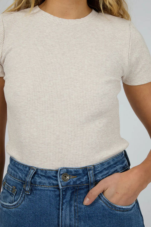 Person wearing a beige ribbed t-shirt and blue jeans against a plain background