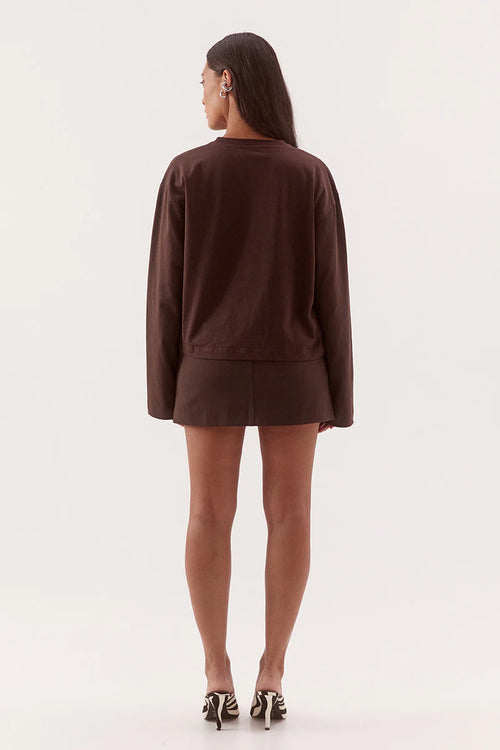 A woman shown from the back wearing a dark brown long-sleeve top and matching mini skirt, paired with black and white patterned heels, against a plain white studio background.