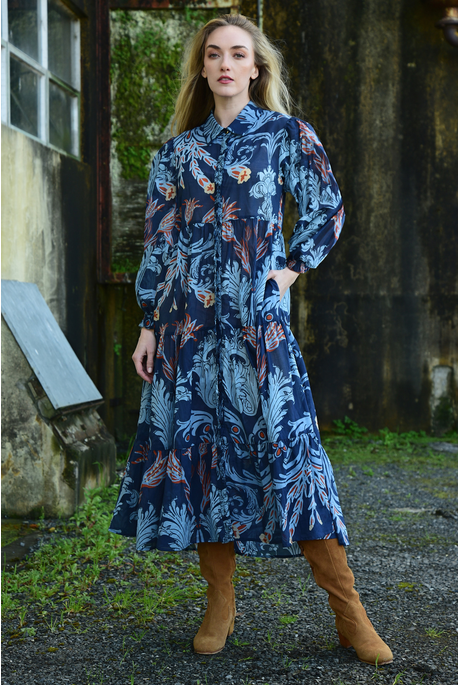 Woman wearing a blue floral dress standing in front of a rustic building.