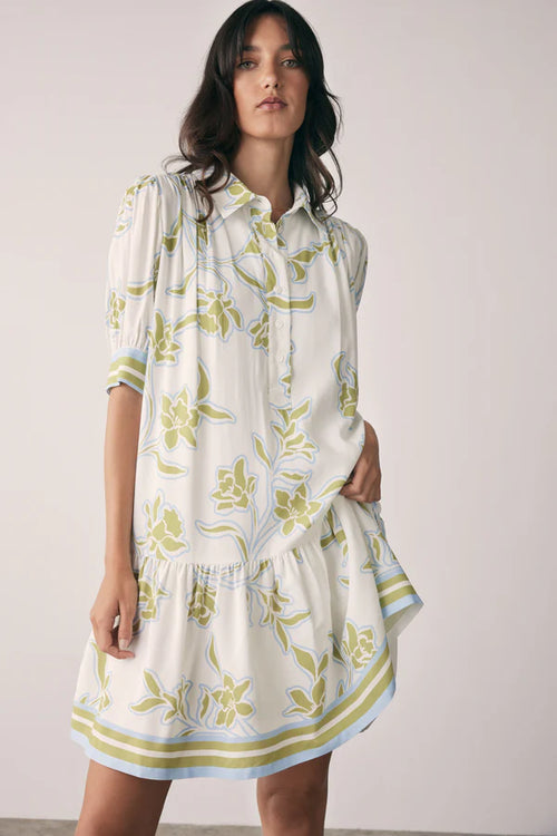 Woman wearing a white dress with green floral pattern against a plain background