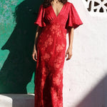 Woman in a red floral dress standing against a white wall with geometric design.