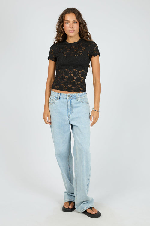 Woman wearing a black lace top and light blue jeans on a white background