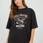Woman wearing a black t-shirt with an eagle graphic and text on a plain background