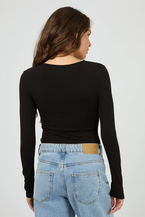 Person wearing a black long-sleeve top and light blue jeans on a plain background