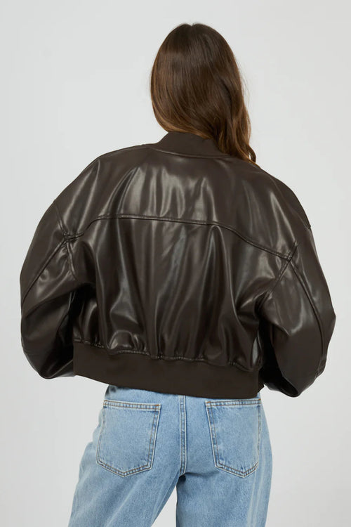 Person wearing a brown leather jacket and blue jeans on a plain background