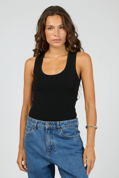 A woman modeling a black scoop-neck tank top paired with blue jeans against a light gray studio background.