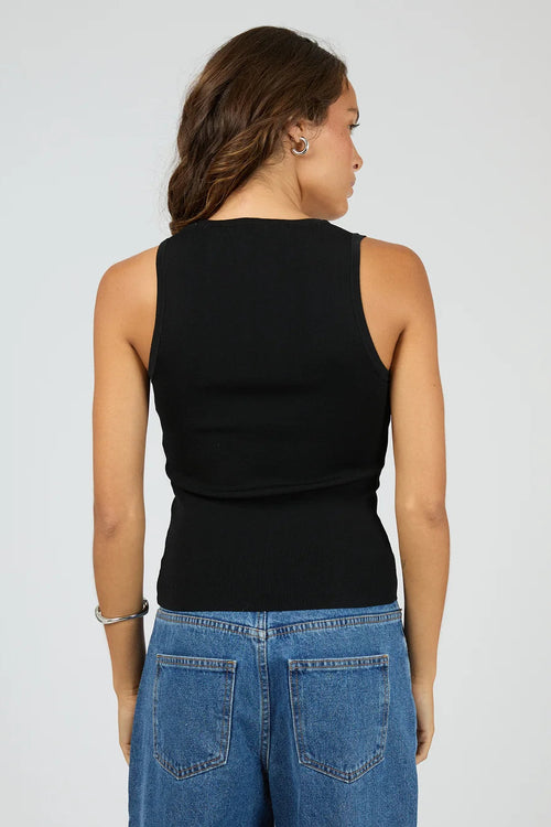 Person wearing a black sleeveless top and blue jeans on a plain background