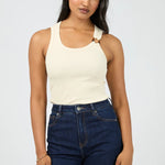 Woman wearing a beige tank top and dark blue jeans against a white background