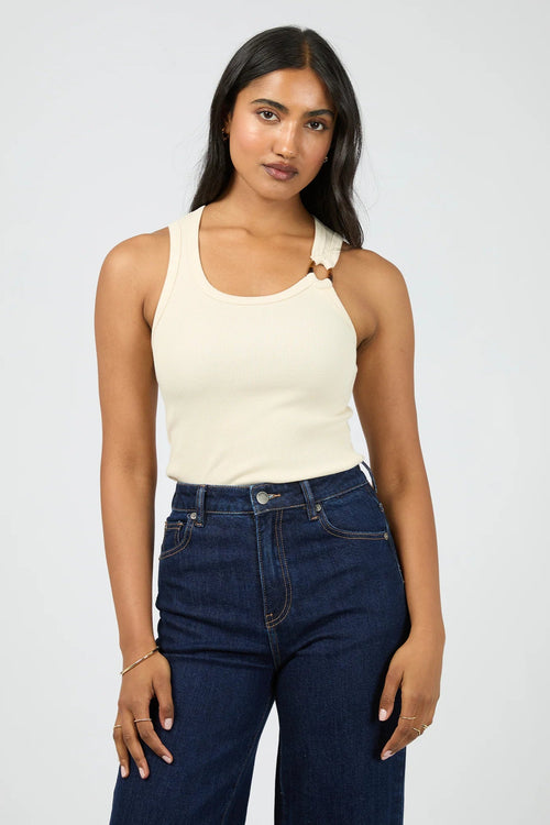 Woman wearing a beige tank top and dark blue jeans against a white background