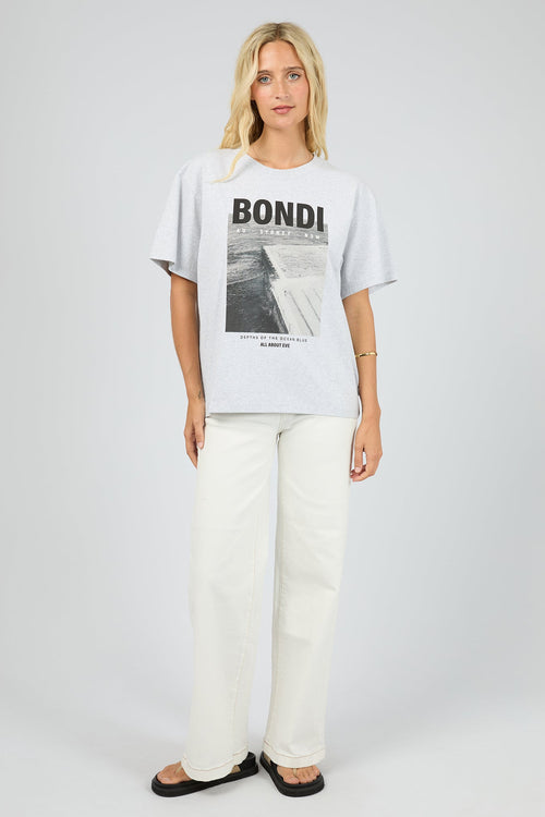 Person wearing a white t-shirt with 'Bondi' print and white pants on a plain background
