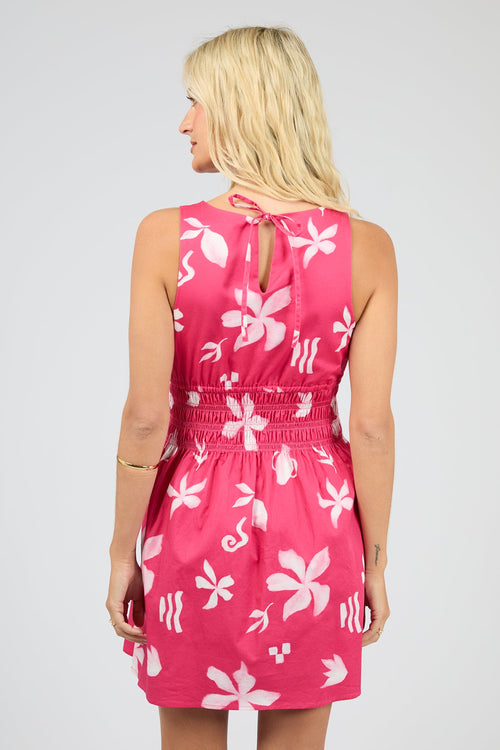 Woman wearing a pink dress with white floral patterns on a plain background