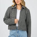 Woman wearing a gray jacket over a white shirt and blue jeans on a light gray background