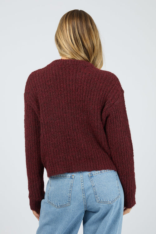 Person wearing a burgundy sweater and blue jeans on a plain background