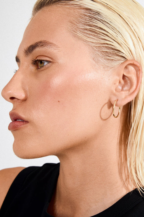 Close-up of a person with blonde hair and hoop earrings on a plain background
