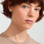 Person with short red hair wearing a beige shirt against a light background