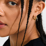 Close-up of a person wearing a gold hoop earring with a plain background