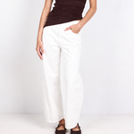 A woman modeling a dark brown off-the-shoulder knit top and white wide-leg pants against a clean white studio background.