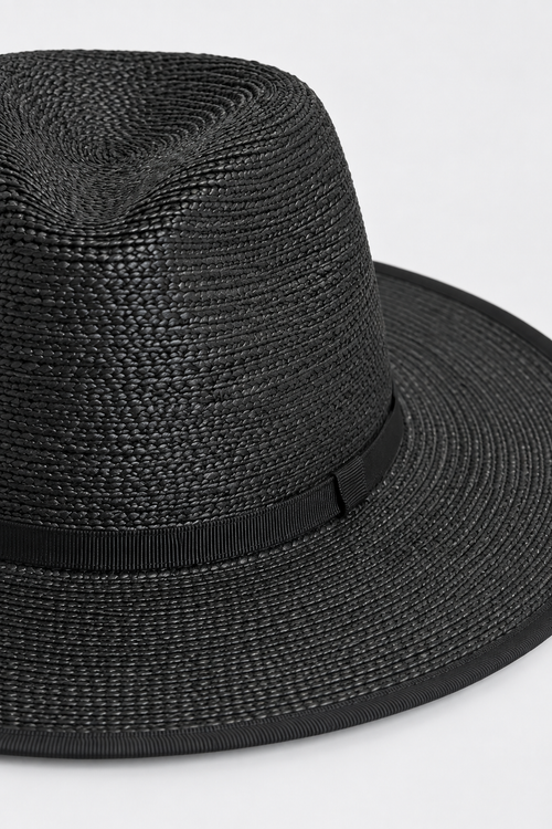 A close-up of a black woven straw fedora hat with a matching black ribbon band, shown against a plain light gray background.