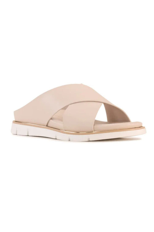 A single women's slide sandal in a light beige or nude color, featuring crisscrossing straps and a low block heel, shown against a plain white background.