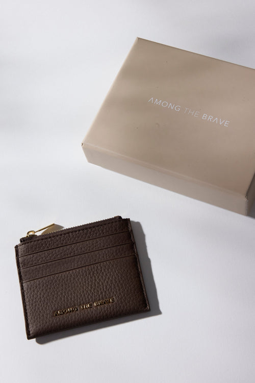 Brown leather wallet with 'Among the Brave' branding on a light gray background