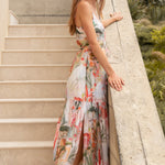 Woman in a floral dress standing on a staircase with greenery in the background