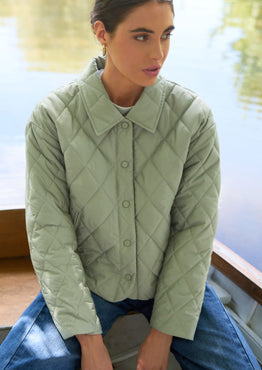 Woman in a green quilted jacket sitting on a boat by a lake