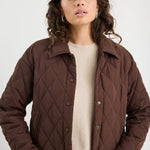 Woman wearing a brown quilted jacket over a beige sweater on a white background
