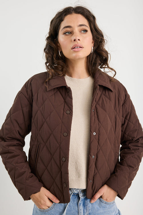Woman wearing a brown quilted jacket over a beige sweater on a white background