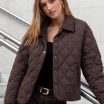 Woman wearing a brown quilted jacket standing on a staircase with a light gray wall background